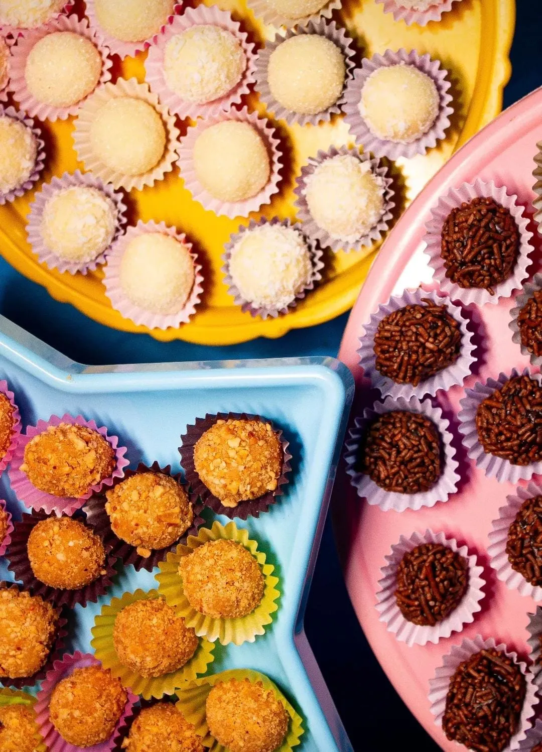 Bandejas coloridas com brigadeiros, beijinhos e docinhos de laranja vistos de cima