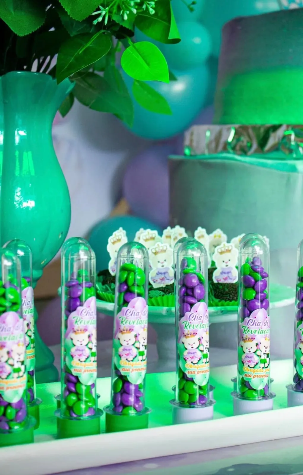 Tubetes de confeitos verdes e lilás com tags personalizadas na mesa da festa