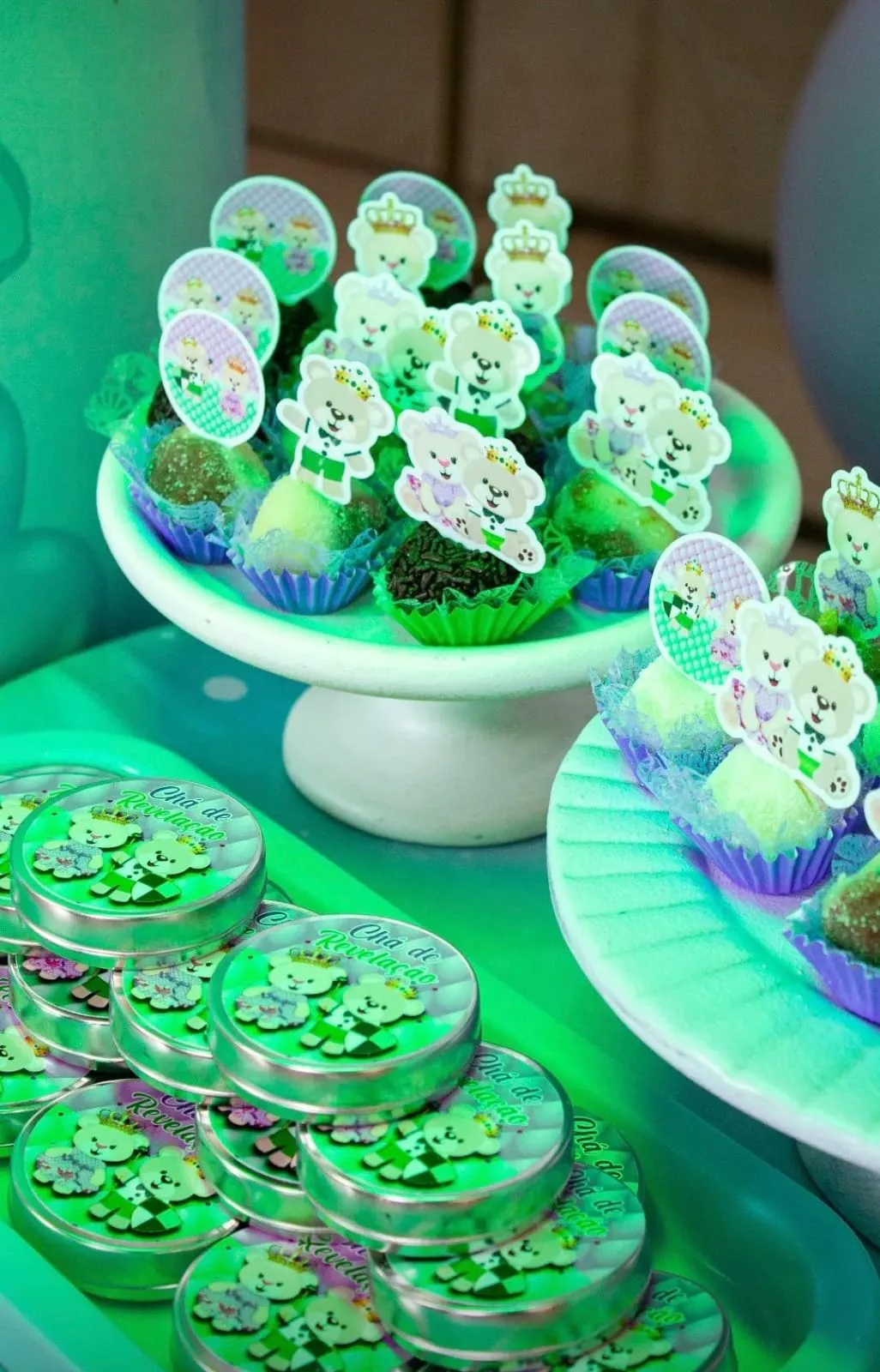 Doces com toppers de ursinhos sobre bandejas brancas, iluminados em verde