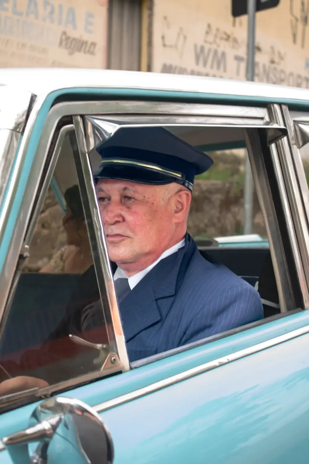 Motorista de terno azul dirigindo o carro antigo