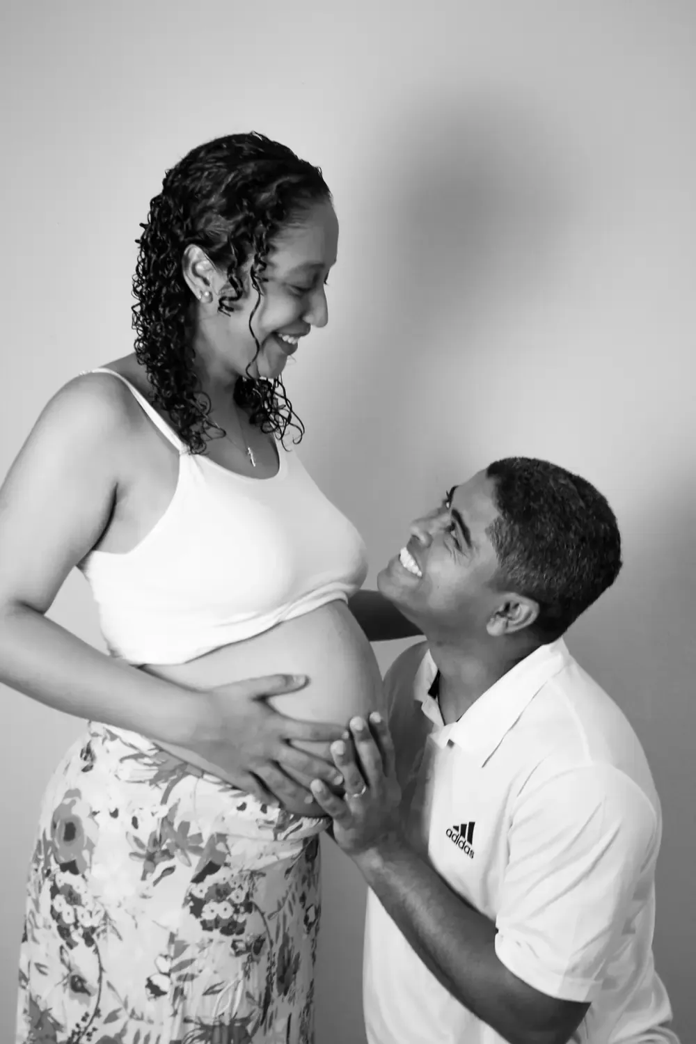 Casal sorrindo em preto e branco, mãos na barriga de grávida