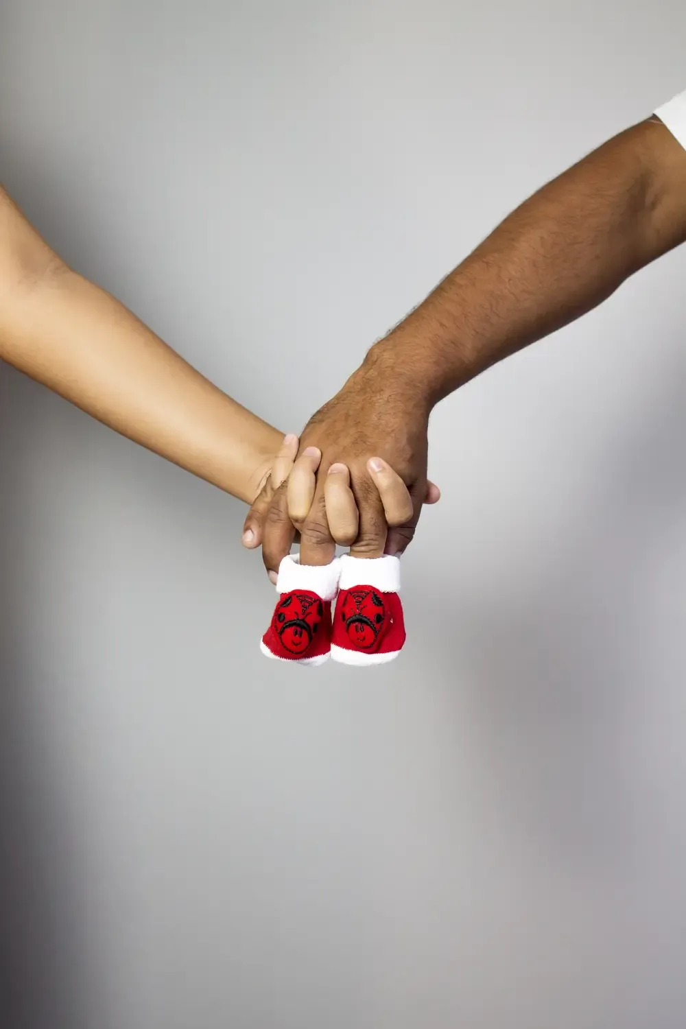 Mãos do casal entrelaçadas segurando os sapatinhos do bebê